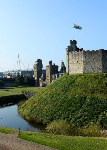 Cardiff castle and the moat with the principality stadium in the background.